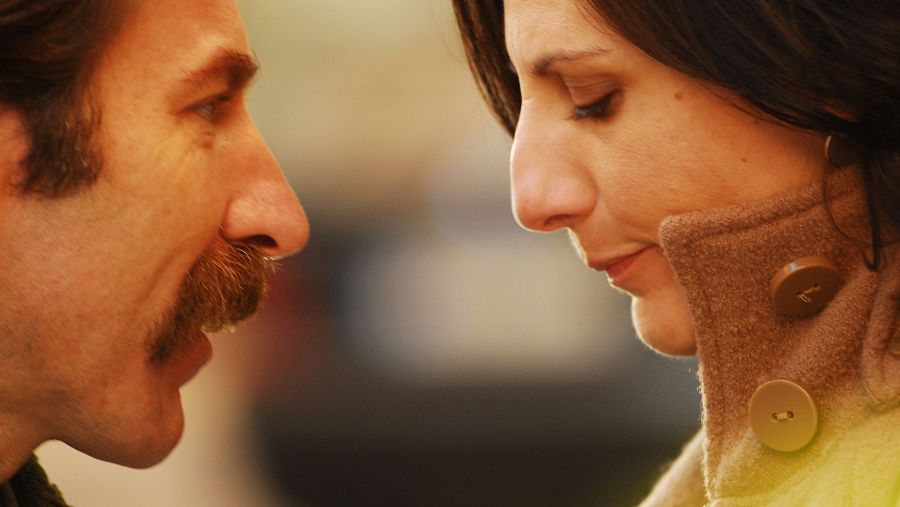 Intensa mirada entre Antonio de la Torre y Malena Alterio. Él viste oscuro, ella un abrigo claro. Fondo desenfocado.