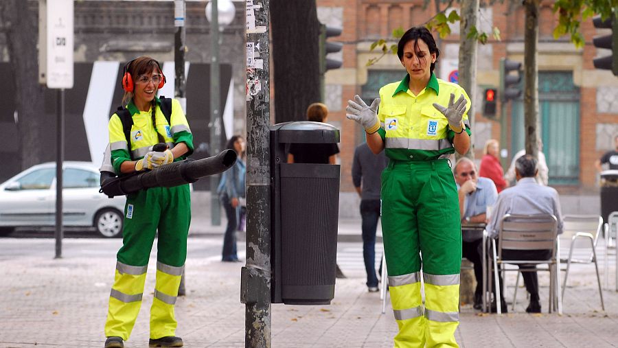 Dos limpiadoras, una con soplador, trabajan en una zona pública con gente al fondo.  En la parte superior: 