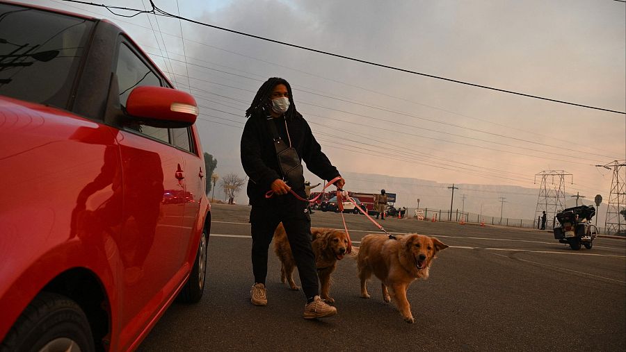 Un ciudadano con dos perros se aleja del humo del incendio Hughes,en el noroeste del condado de Los Ángeles