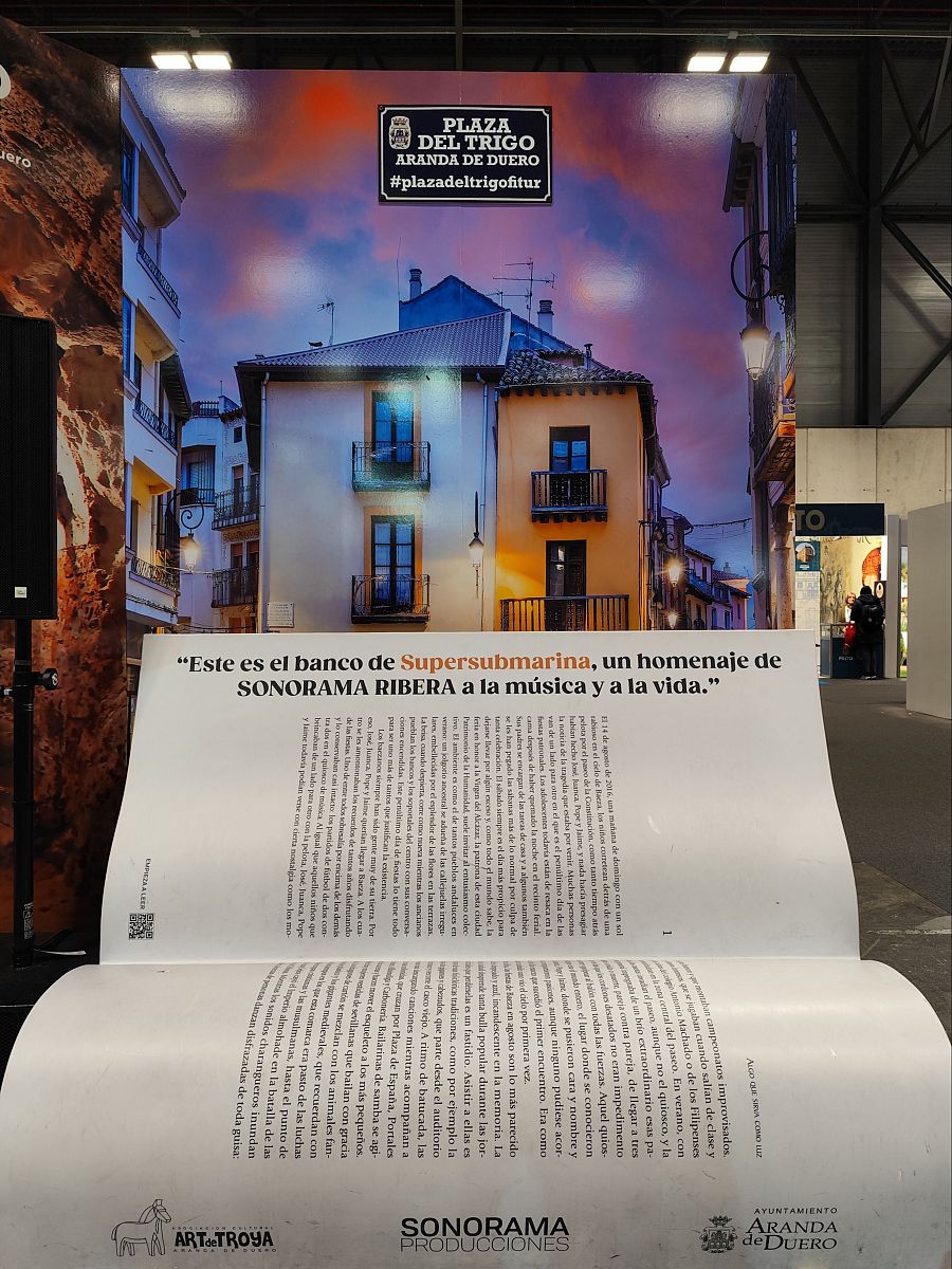 Banco gigante en forma de libro abierto proyectando una imagen de una plaza. Homenaje musical con logos de Sonorama Producciones y el Ayuntamiento de Aranda de Duero.