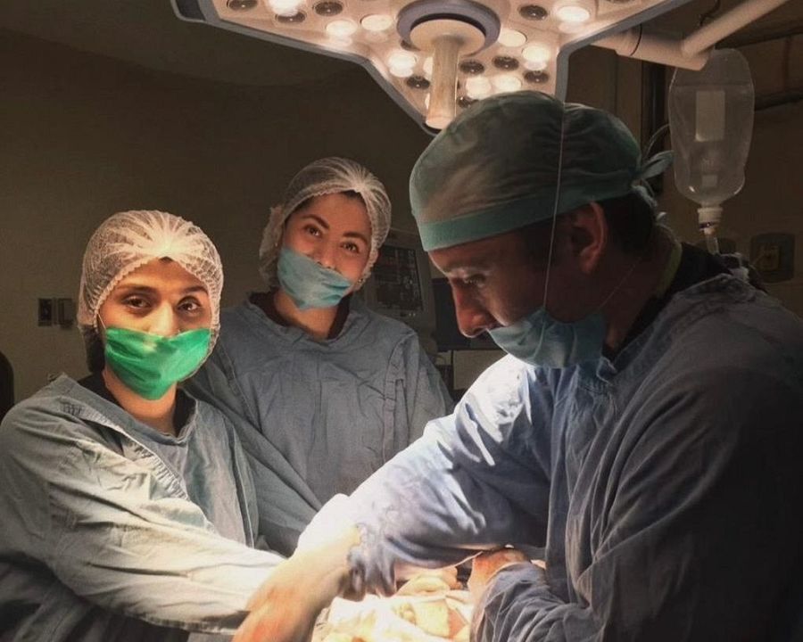 Quirófano mexicano. Un cirujano y dos mujeres, vestidas con atuendos quirúrgicos, durante una intervención. Iluminación intensa.