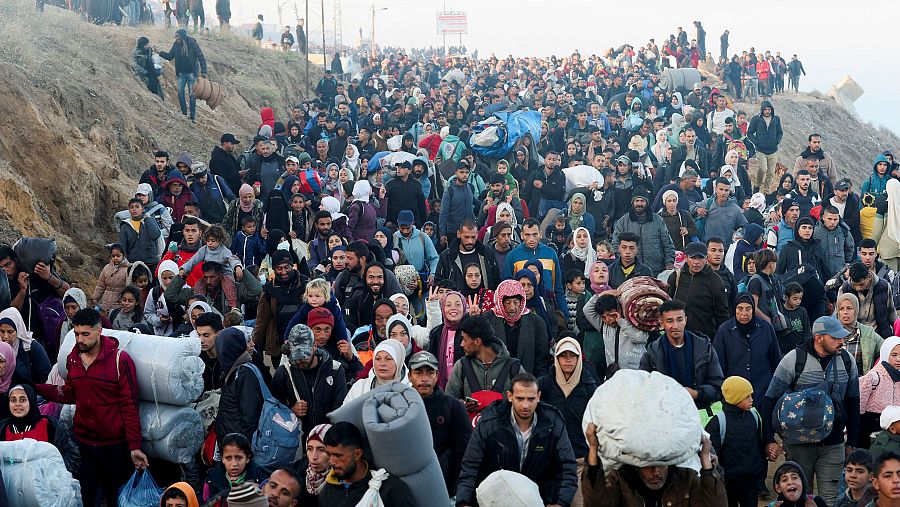 Personas de todas las edades caminan por un camino, llevando consigo sus pertenencias.  La imagen evoca un regreso a casa tras un desplazamiento forzado.