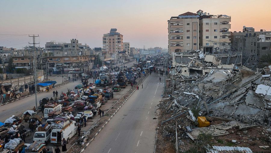 Vehículos abarrotados en una carretera, algunos cargados.  Edificios destruidos junto a otros intactos.  Atmósfera de retorno tras un evento devastador.