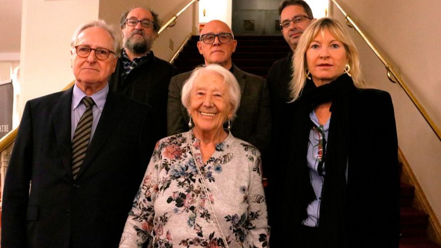 Teresa Cunillé y otras cinco personas, posiblemente propietarios y jurado de un premio, posan en un teatro junto a una escalera con barandilla dorada y alfombra roja.