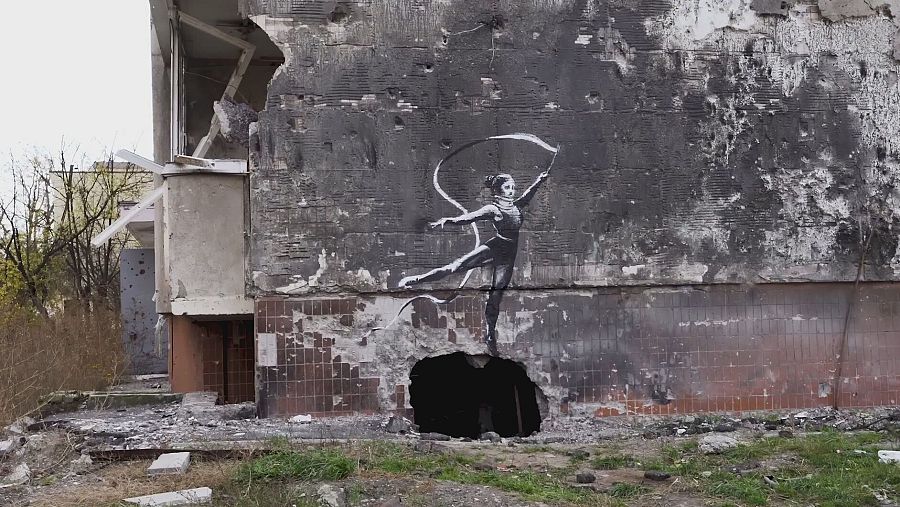 Grafiti de una bailarina en movimiento sobre una pared dañada por bombardeos.  La imagen contrasta la fragilidad del arte con la brutalidad de la destrucción.