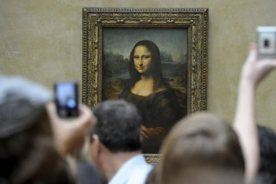 Turistas fotografiando la Mona Lisa en el Louvre.  Mucha gente observa el cuadro desde atrás, creando una escena de gran afluencia.