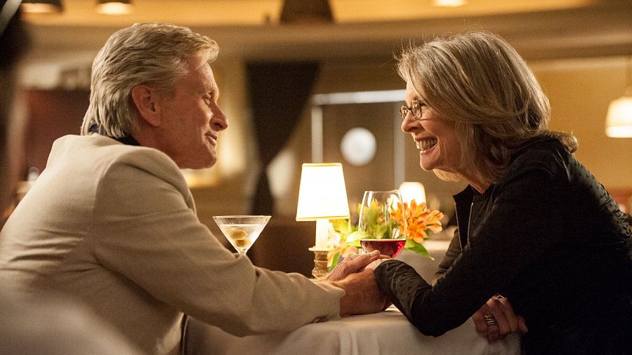 Escena romántica de 'Así nos va' con Michael Douglas y Diane Keaton sentados a una mesa, cogidos de la mano y compartiendo bebidas.
