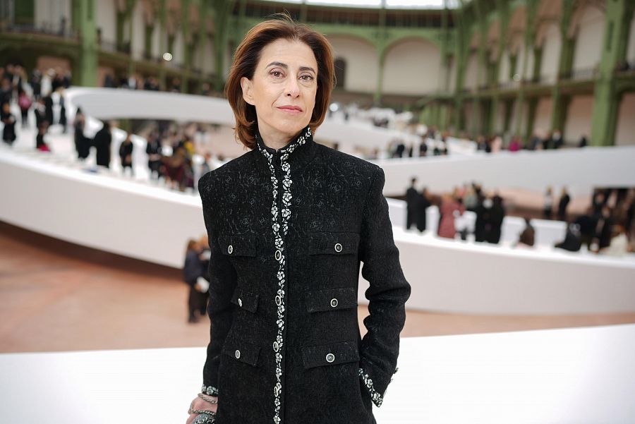 Actriz con chaqueta negra y detalles plateados en evento concurrido. Cabello corto castaño.  Ambiente interior amplio.