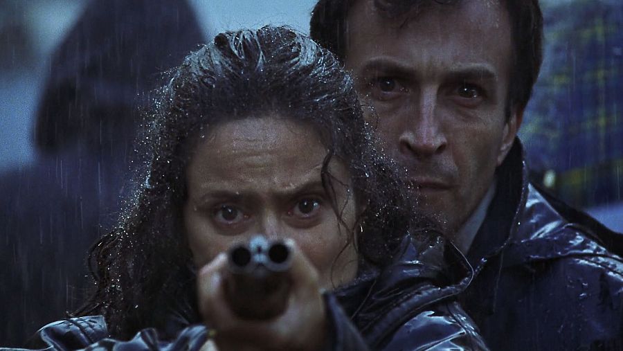 Imagen de Aitana Sánchez Gijón con una escopeta y Daniel Giménez Cacho detrás de ella, en Celos, de Vicente Aranda