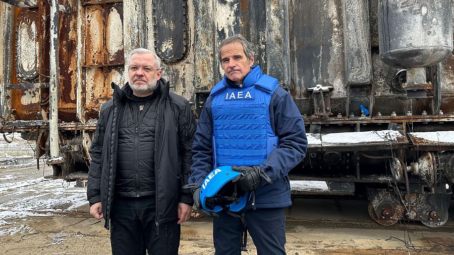 Inspección de daños en una estructura metálica, posiblemente un transformador, en una zona nevada.  Un hombre con chaleco antibalas con logo y casco inspecciona la zona con un acompañante.