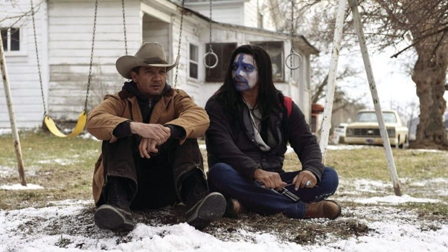 Jeremy Renner y Gil Birmingham sentados sobre la nieve en la película Wind River