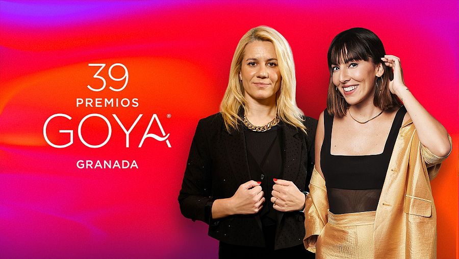Dos actrices, una con chaqueta negra y collar dorado, la otra con un conjunto dorado y blusa negra, posan en una alfombra roja con el logo de los Premios Goya 39.