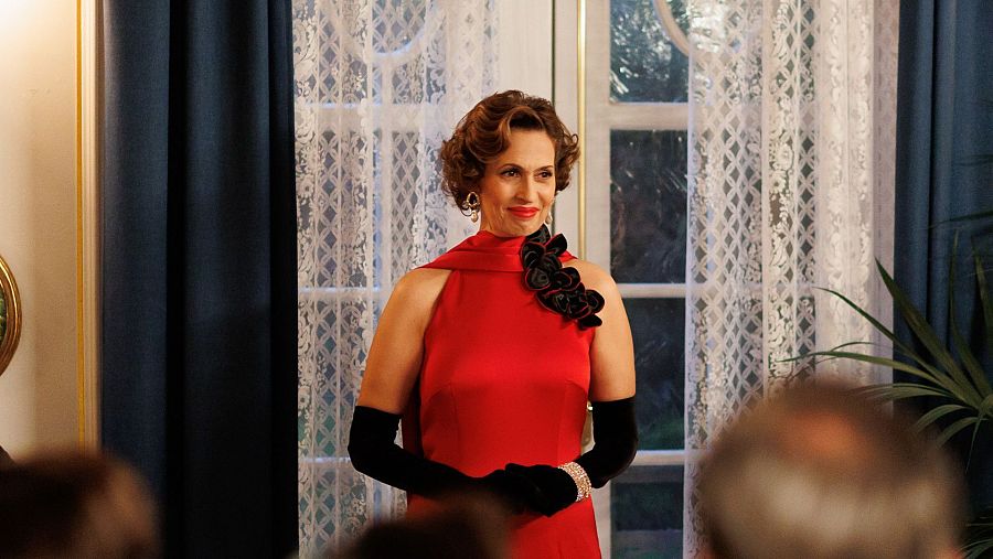 Elegante mujer de vestido rojo declara su amor en una recepción.  Fondo con cortinas y detalles decorativos.
