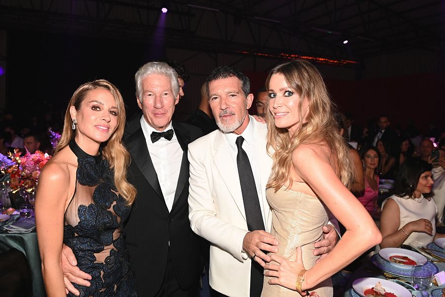 Cuatro personas elegantemente vestidas sonríen a la cámara en un salón de eventos.  Se aprecian vestidos largos, esmoquin y trajes, con un ambiente formal.