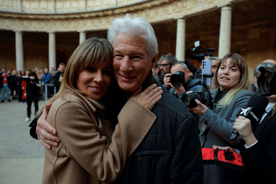 Richard Gere y Alejandra Silva abrazados, sonrientes, rodeados de fotógrafos y cámaras en un evento público.