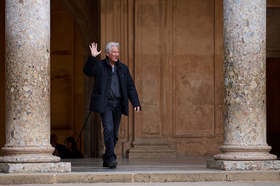 Richard Gere saluda desde el Palacio de Carlos V, en Granada. Viste traje oscuro y se le ve caminando entre columnas de piedra.