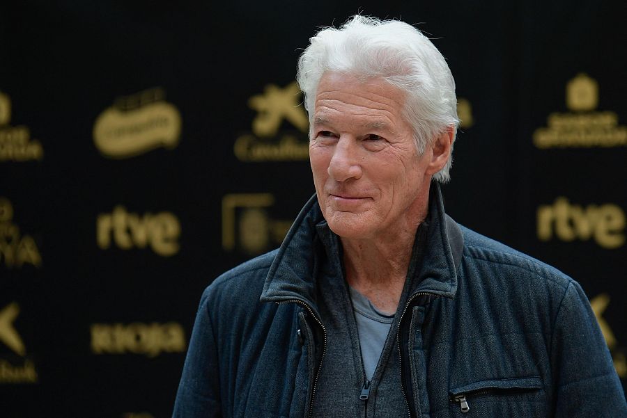 Richard Gere, con chaqueta oscura, sonríe levemente en una imagen con fondo negro y logotipos, entre ellos RTVE, en el Palacio Carlos V de Granada.
