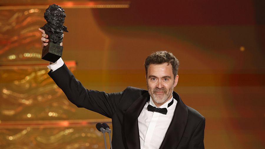 Director en esmoquin, sonriente, alza el premio Goya a la mejor dirección.  Emoción en la ceremonia de entrega de premios.