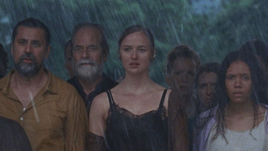 Intensa escena bajo la lluvia en 'La tutoría', mostrando a un grupo de personas con expresiones serias. Fondo oscuro y borroso.