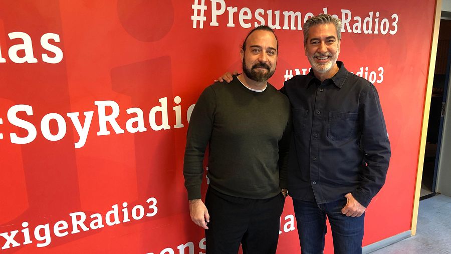 Dos hombres sonríen para una foto promocional de Radio 3 en la sede de RNE. Uno lleva jersey verde y el otro camisa oscura.