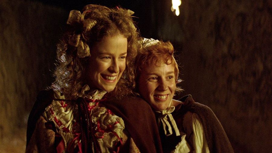 Dos mujeres con atuendos de época sonríen en una escena oscura, posiblemente una cueva, de la película 