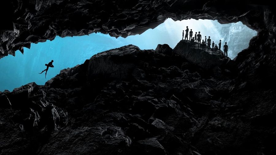 Siluetas de buzos en una cueva submarina oscura, durante una operación de rescate.  Agua azul brillante visible en la entrada.