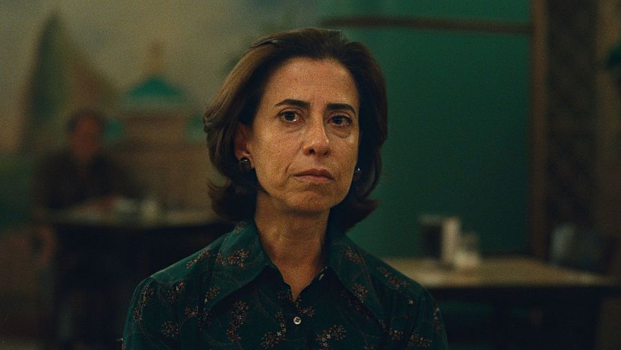 Fotografía de Fernanda Torres con expresión seria, camisa verde oscura, en un ambiente de cafetería o restaurante. Posible foto promocional o escena de 'Aún estoy aquí'.