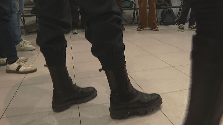 Diversos pies y piernas con distintos calzados (botas, zapatillas) en una reunión.  Perspectiva enfocada en los pies, mostrando anonimato.