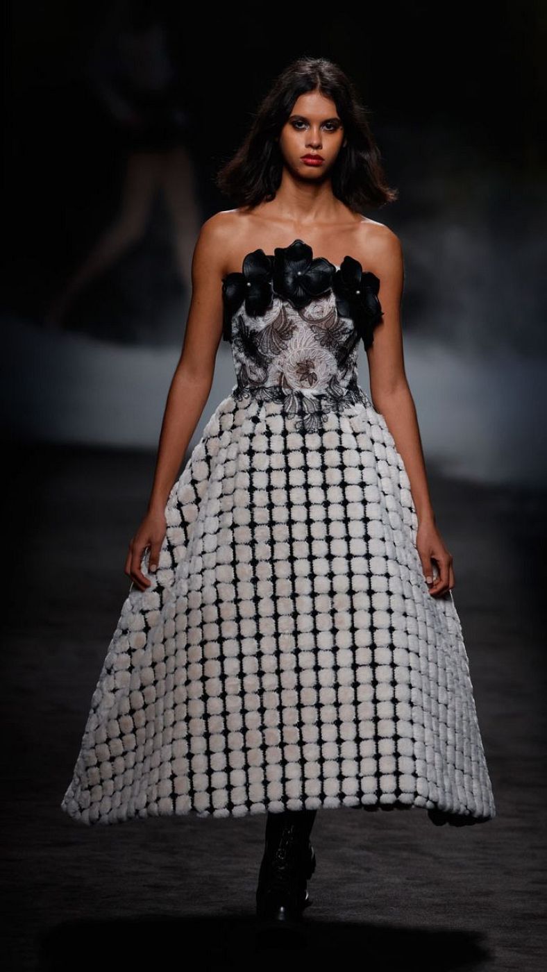 Modelo de pelo corto y oscuro desfila con un vestido negro y blanco de Yolancris; la parte superior es negra semitransparente bordada y la falda acampanada es blanca con círculos en relieve.