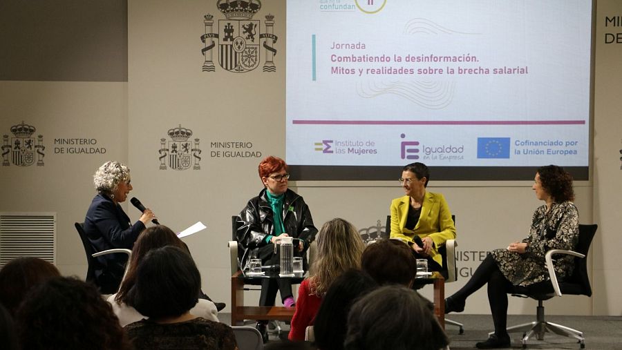 Cuatro mujeres discuten la brecha salarial en una jornada, combatiendo la desinformación con datos y estadísticas.  Se ven logos del Ministerio de Igualdad y la UE.