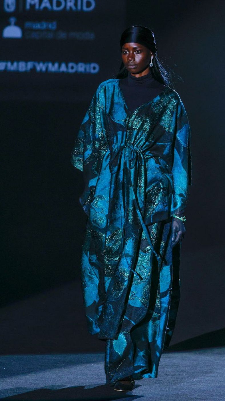 Caftán azul oscuro con estampado abstracto, jersey negro, turbante y guantes.  Brazalete verde y estética boho setentera.