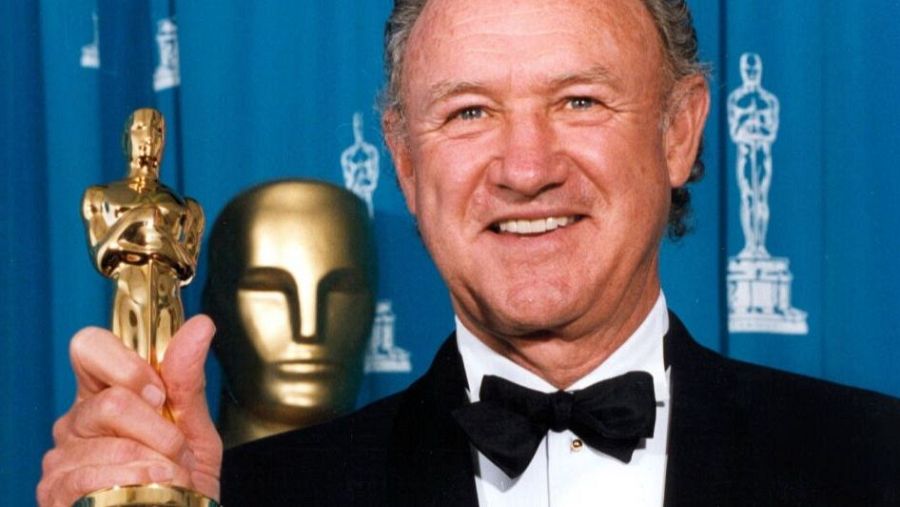 Actor con esmoquin sosteniendo un Oscar y sonriendo a cámara; dos estatuillas más al fondo.  Imagen que celebra un premio.