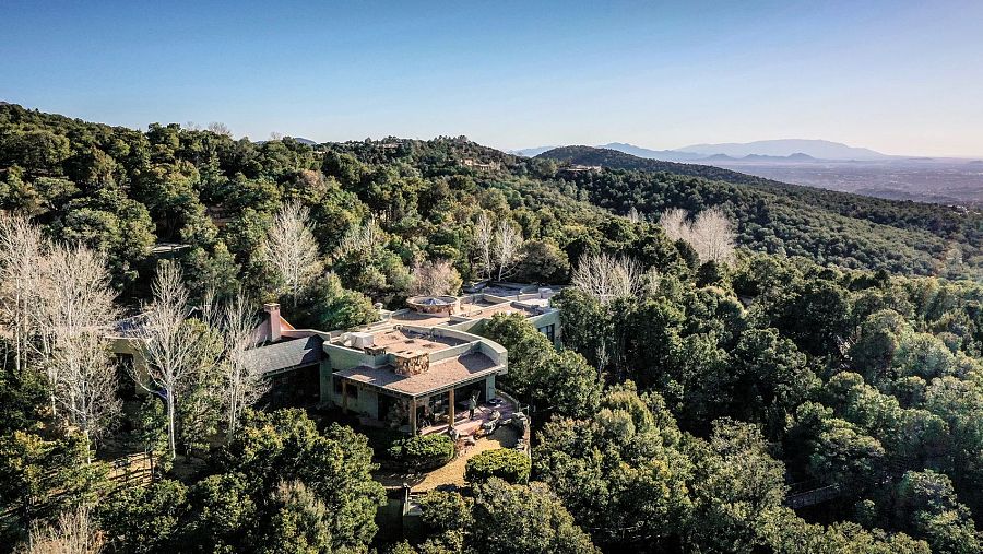 Vista aérea de una casa en una ladera, con tejado de teja y abundante vegetación otoñal.  La casa tiene varios niveles y una terraza, integrándose en el paisaje montañoso.