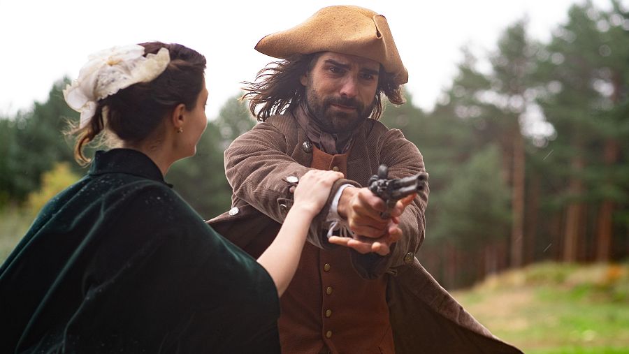 Dos personajes de época, él con tricornio y pistola, ella con vestido verde, en un bosque.  Escena de acción.