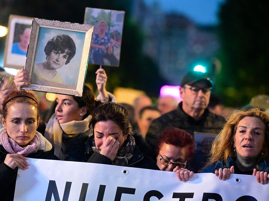 Ciudadanos valencianos protestan mostrando imágenes de afectados por la DANA.  Se aprecia tristeza y una pancarta con la palabra 