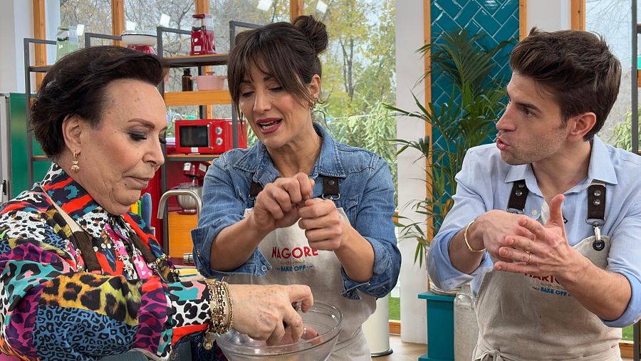 Tres participantes de 'Bake Off: famosos al horno' con delantales, en una escena de cocina. Uno gesticula, otro manipula ingredientes y el tercero observa.