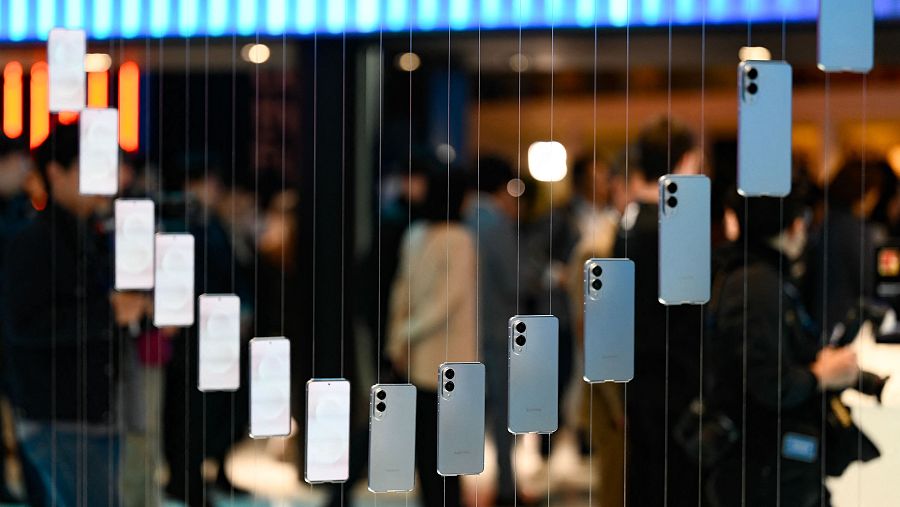 Exhibición de teléfonos Samsung Galaxy S25 Edge colgando en diagonal, creando una cascada visual.  Público desenfocado al fondo.