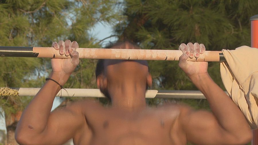 Joven haciendo dominada en barra, con magnesio en las manos y pulsera.  Forma parte de una serie de retos o reportajes.