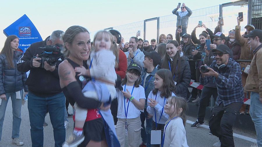 Verdeliss, feliz y con su bebé en brazos, celebra con su familia tras cruzar la meta de una carrera, rodeada de apoyo y atención.