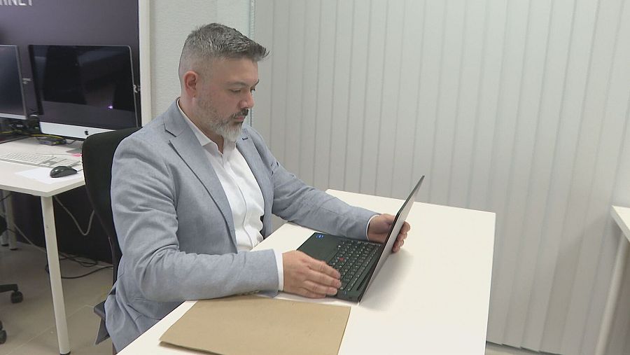 Investigador sentado en una oficina moderna usando un portátil.  Ambiente de trabajo limpio y ordenado con otros ordenadores visibles.