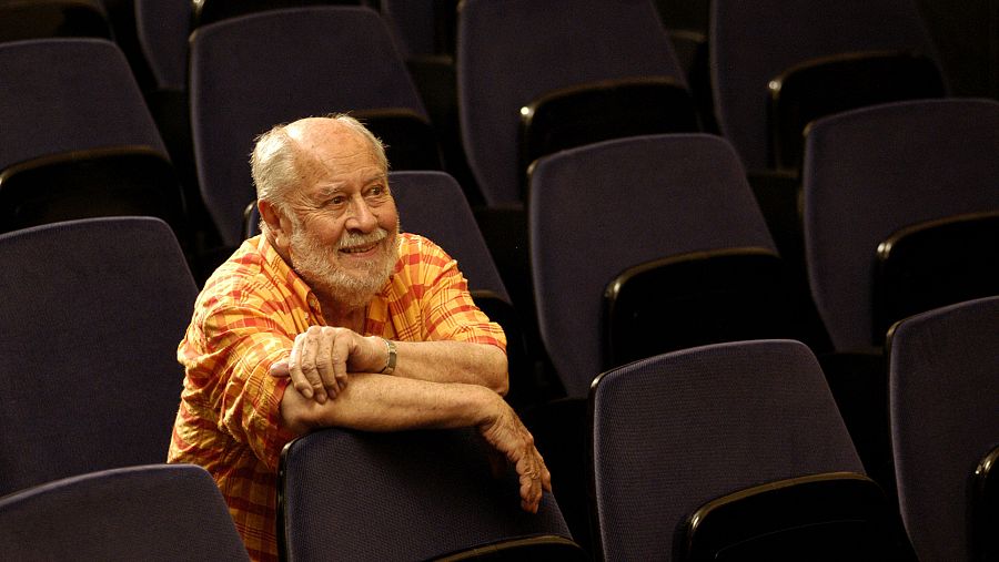 Jaime de Armiñán, sonriente y con camisa a cuadros, sentado en una butaca de un auditorio. Iluminación tenue, butacas vacías al fondo.