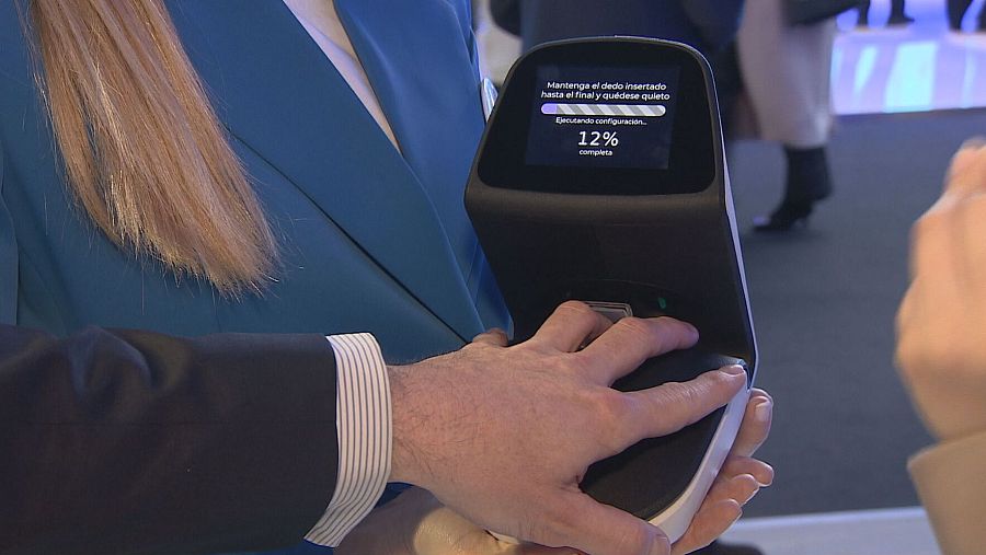 Configuración inicial de un dispositivo PointCheck: una persona coloca su dedo en el escáner, la pantalla muestra un 12% de progreso y un mensaje de instrucciones.