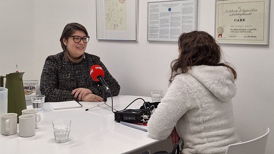 Entrevista a la presidenta del Consejo Circumpolar Inuit. Se observa a la entrevistada sentada a una mesa con una periodista, micrófono, grabadora y varios objetos sobre la mesa.