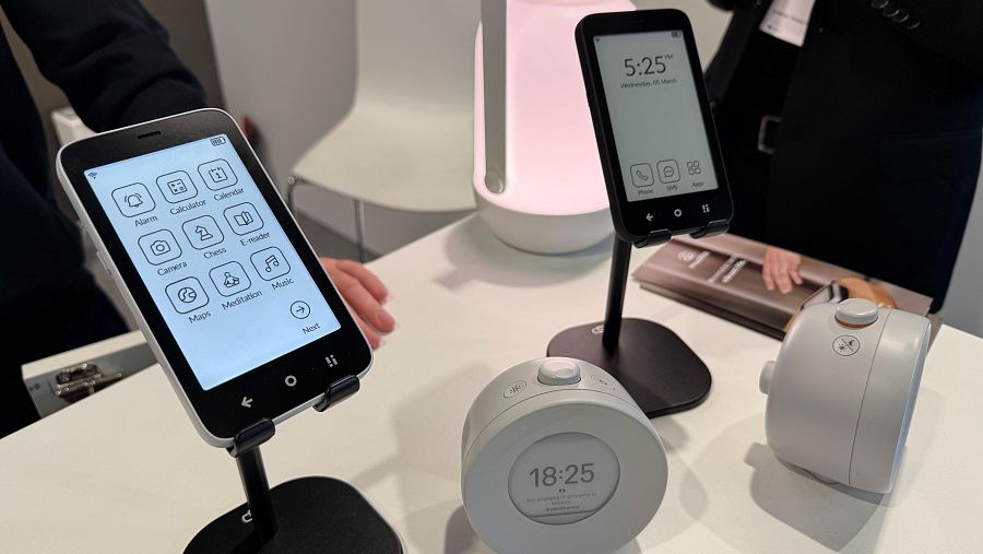 Imagen de tres dispositivos Mudita: dos teléfonos (uno mostrando iconos de apps y otro la hora) y un posible reloj/altavoz con pantalla circular. Diseño minimalista en blanco y negro.