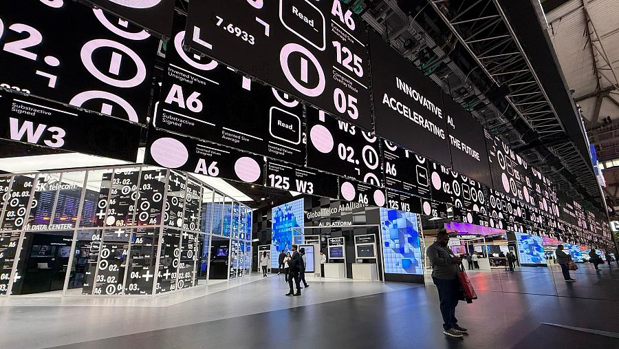 Pabellón tecnológico con múltiples pantallas mostrando datos, gráficos y textos relacionados con IA y supercomputación; personas interactúan con el entorno.