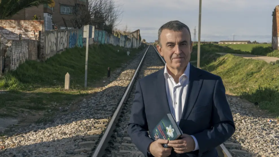 Lorenzo Silva presenta 'Las fuerzas contrarias'.  El autor posa con su libro en un entorno que combina paisaje urbano y vías de tren.