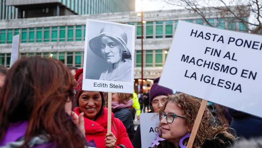 Una mujer lleva una pancarta con la que pide la igualdad en la Iglesia y otra, una imagen de la filósofa Edith Stein.