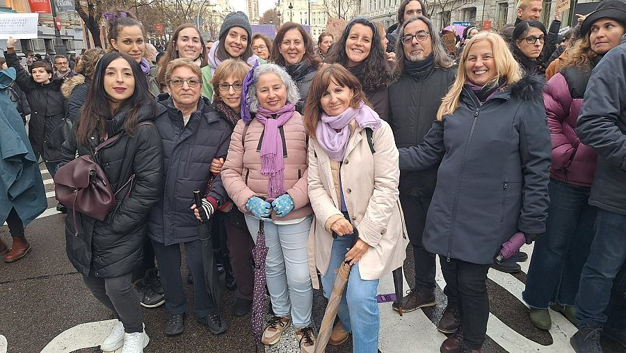 Mujeres en manifestación o concentración posan para una foto en una calle. Visten ropa oscura con detalles morados y rosas. Fondo urbano.