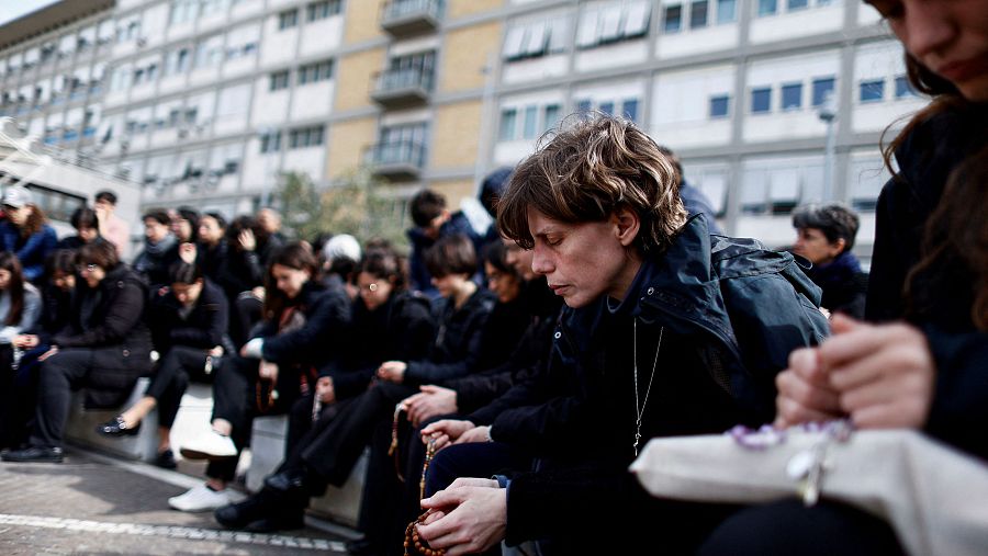 Un grupo de personas reza junto a la estatua del difunto Papa Juan Pablo II a las puertas del hospital Gemelli.