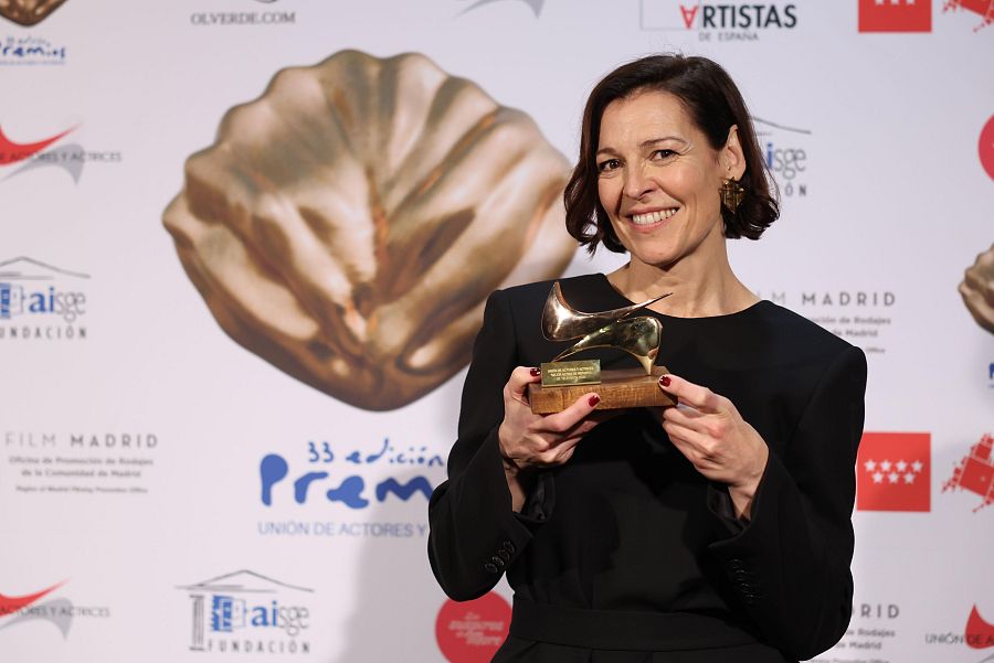 Actriz sonriendo con premio en forma de zapato de tacón, en un photocall con fondo blanco y logos.  33ª edición Premios Unión de Actores.